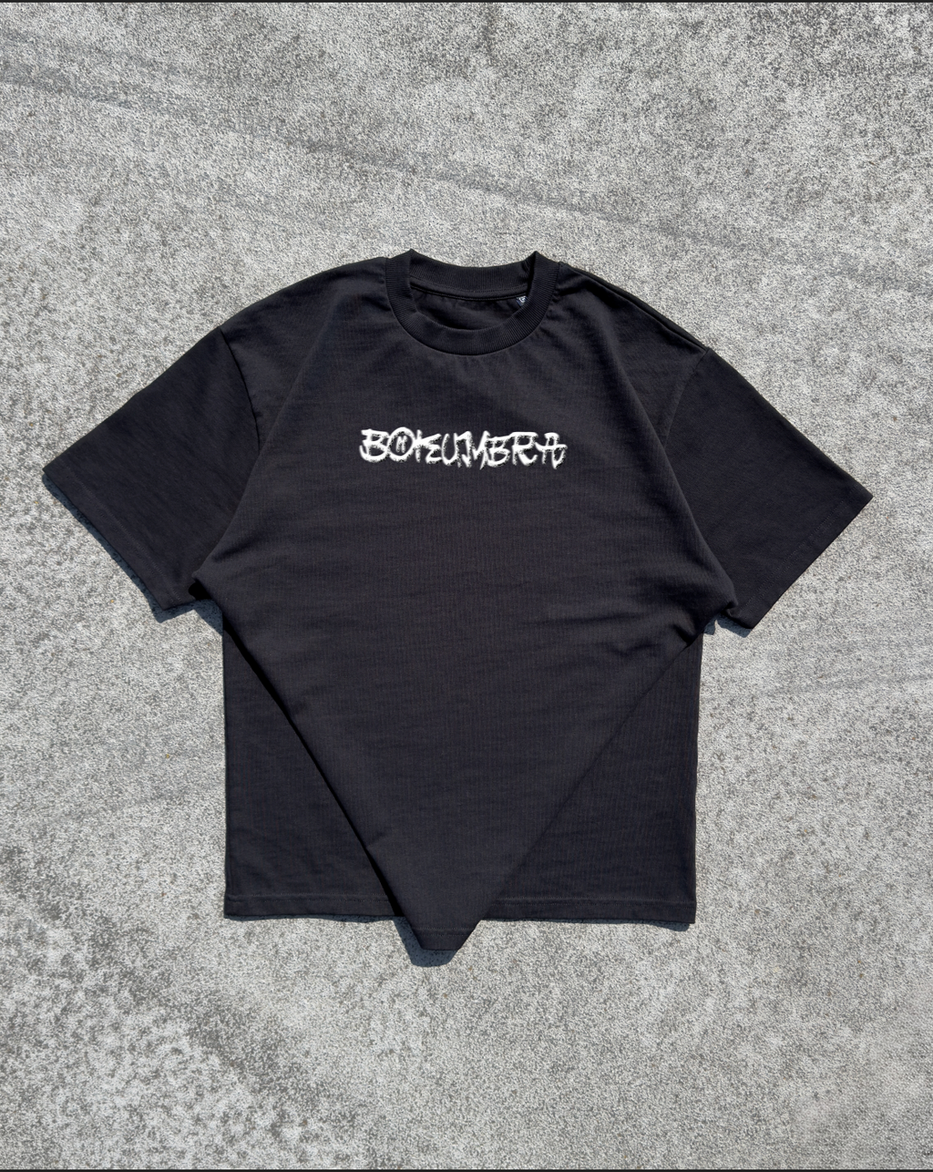 A black short-sleeve t-shirt with the word 'BOKEMERIT' printed in a stylized white gothic font across the chest, laid flat on a textured gray concrete surface.