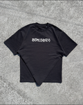 A black short-sleeve t-shirt with the word 'BOKEMERIT' printed in a stylized white gothic font across the chest, laid flat on a textured gray concrete surface.