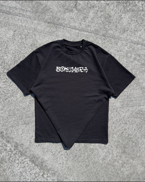A black short-sleeve t-shirt with the word 'BOKEMERIT' printed in a stylized white gothic font across the chest, laid flat on a textured gray concrete surface.