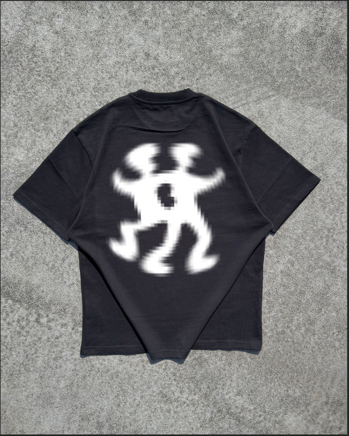 A black short-sleeve t-shirt laid flat on a textured gray concrete surface, showing a large white graphic print on the back depicting a dancing figure.