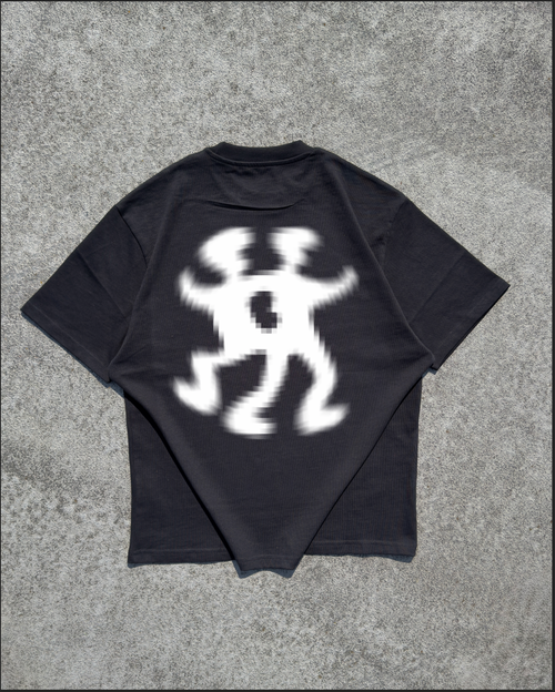 A black short-sleeve t-shirt laid flat on a textured gray concrete surface, showing a large white graphic print on the back depicting a dancing figure.